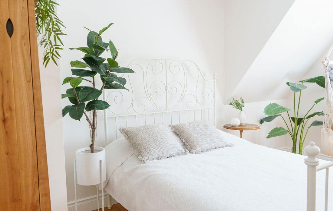 Chambre blanche avec lit et plantes artificielles - Décors Véronneau