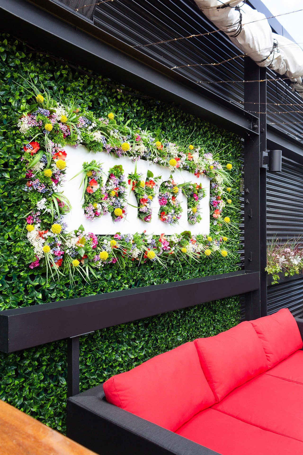 Mur végétal floral extérieur composé de fleurs colorées et de verdure artificielles vibrante allant avec le concept même du décor thématique de cette terrasse sur le toit. - Décors Véronneau