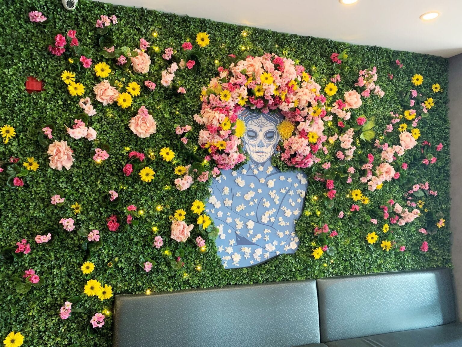 Mur de buis et de fleurs artificielles incluant le personnage La Catrina dont les cheveux sont composés de fleurs artifiicelles - Décors Véronneau