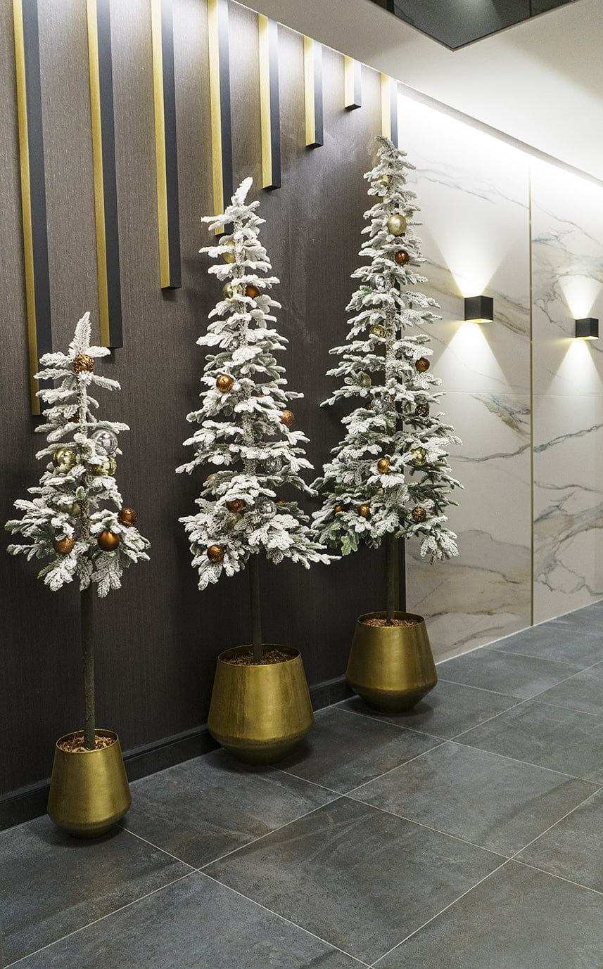 Trois petits sapins alpins enneigés de différentes grandeurs dans des pots métalliques disposés dans l'espace commun de cet édifice. - Décors Véronneau